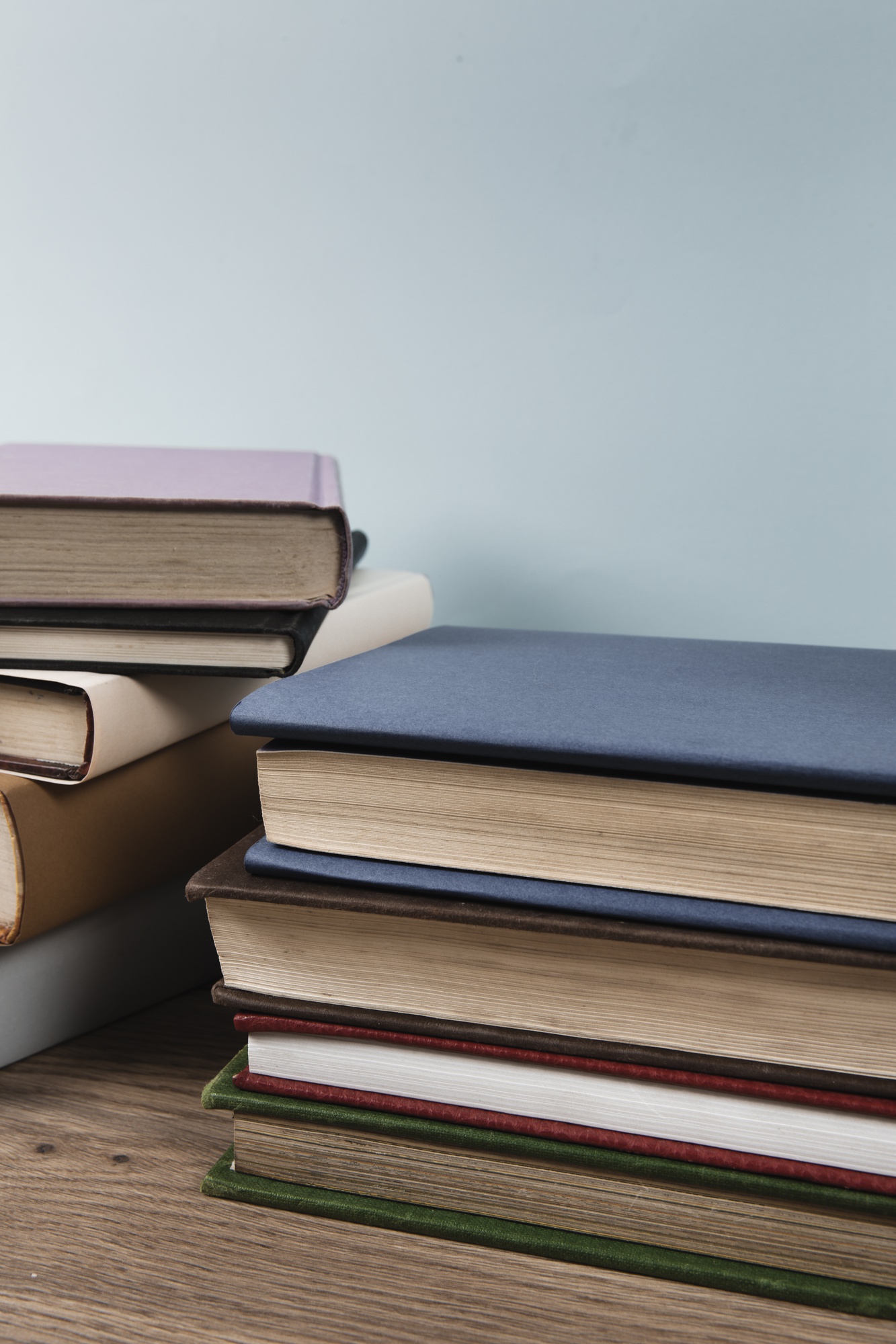 Pilha de livros de capa dura em tons variados, empilhados sobre uma mesa de madeira.